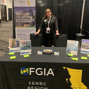 Amy Roberts standing behind the FGIA FENBC Region table at Top Glass with a banner behind her