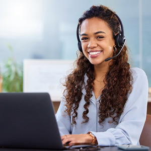 woman with long brown curly hair in blue shirt with headset using laptop in an office setting